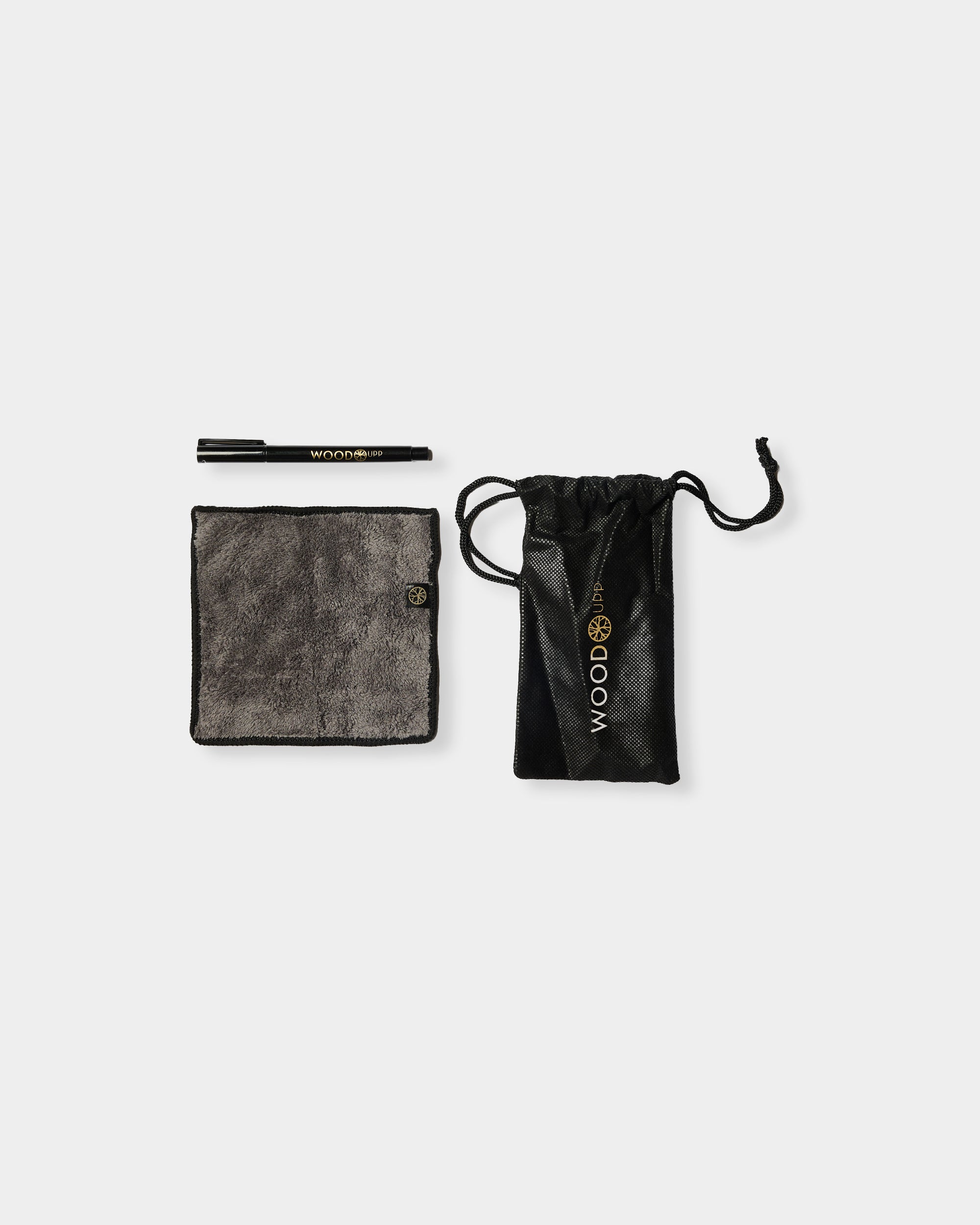 A black pen, gray microfiber cloth, and black drawstring pouch with gold “WOOTBOX” branding arranged on a plain white background.